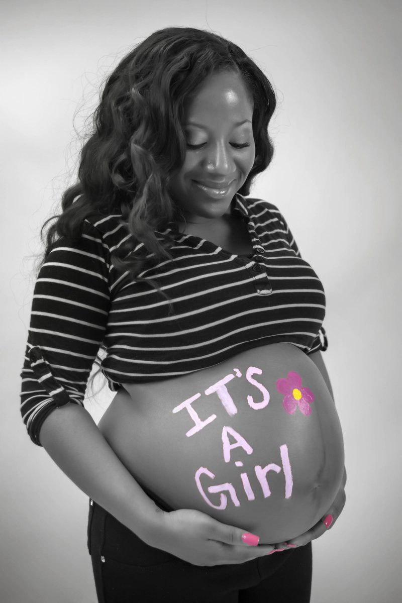 Black-and-white maternity portrait with 'It's a girl' painted on the belly