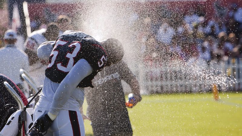 Football player cooling off under a water spray at training camp