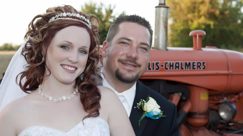 Bride and groom smiling beside a red Allis-Chalmers tractor